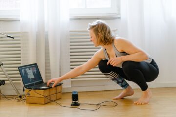 Yogalehrerin Christiane Havenith hockt sich vor dem Laptop runter, um die Teilnehmenden der Online-Yogastunde zu begrüßen