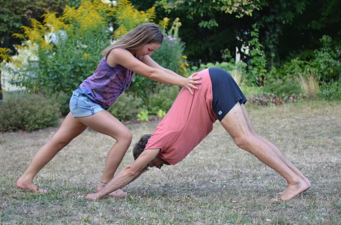 Yogalehrerin Louisa gibt einem Yoga-Teilnehmer Hands-On im Herabschauenden Hund