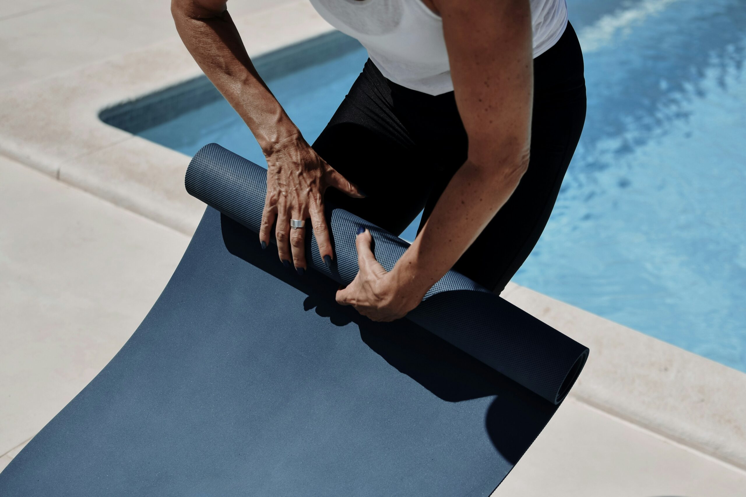 ein Mann hält eine Yogamatte in der Nähe eines Swimmingpools