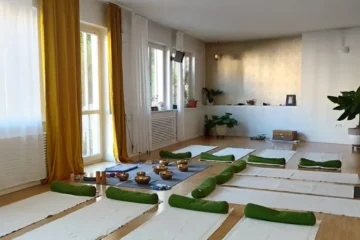 Ein heller freundlicher Yogaraum, in dem Yogamatten und Kissen sowie Klangschalen ausliegen für ein Sound Bath und Klangmassage im Yogastudio Fuß über Kopf