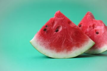 Zwei Stücke Wassermelone vor einem türkisfarbenem Hintergrund.