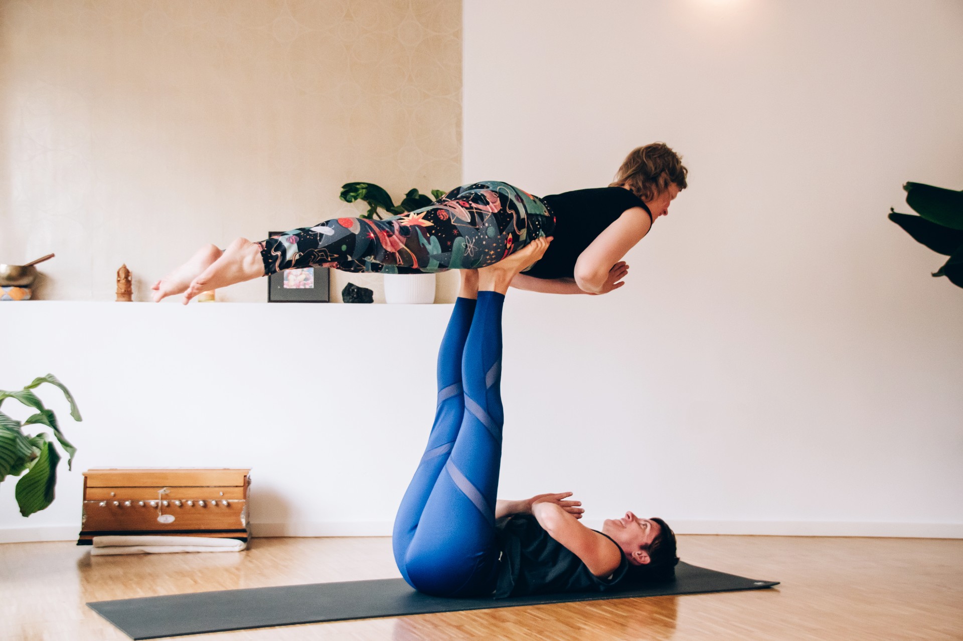 Yogalehrerin Simone liegt in Rückenlage und trägt Yogalehrerin Christiane auf den Füßen beim Acro-Yoga im Fuß über Kopf Yogastudio